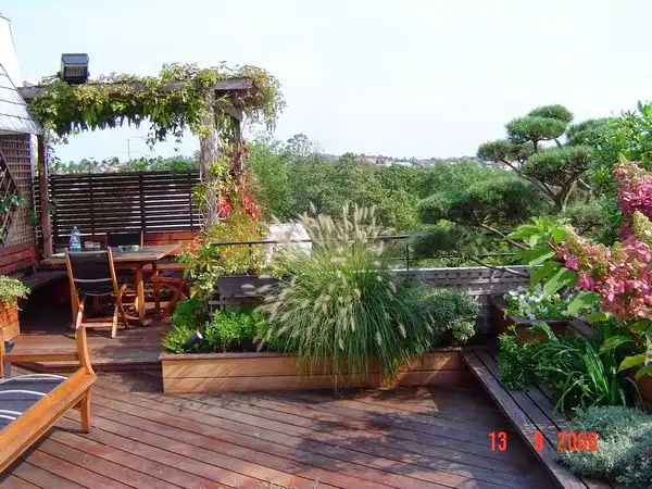 Terrasse en bois végétalisée avec espace repas, pergola et massifs de graminées